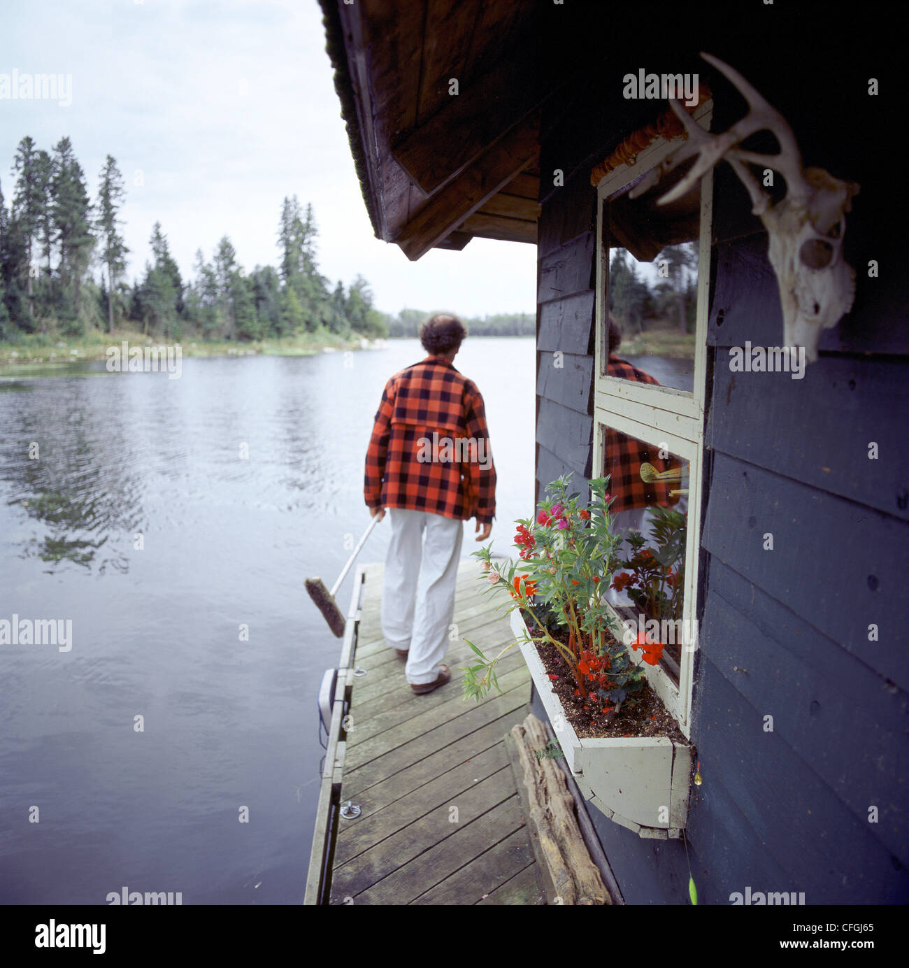 Man Walking with Broom on Cabin Dock by Lake, Gunn Lake, Minaki