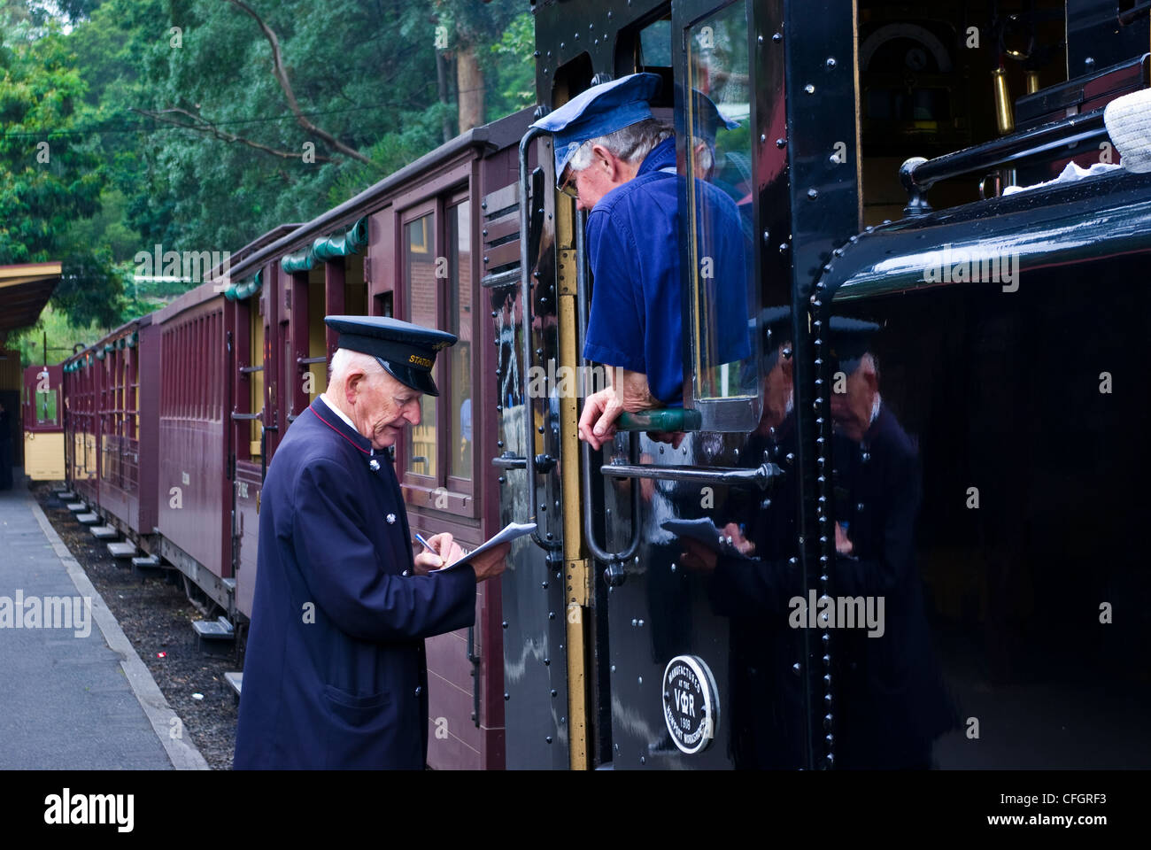 The station master confirms timetables with a steam train driver. Stock Photo