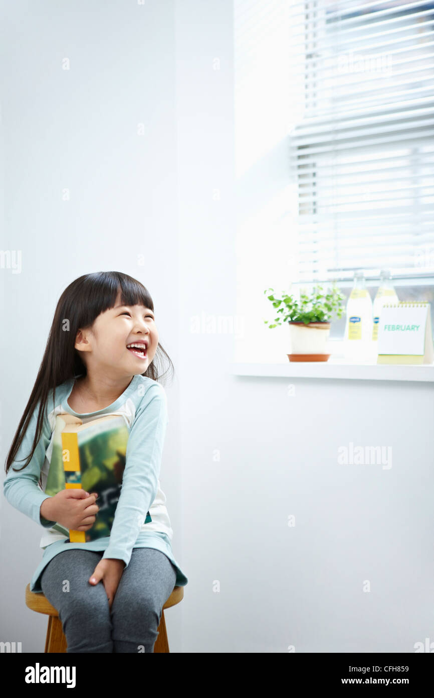 The girl with big smile holding a book on the chair Stock Photo - Alamy