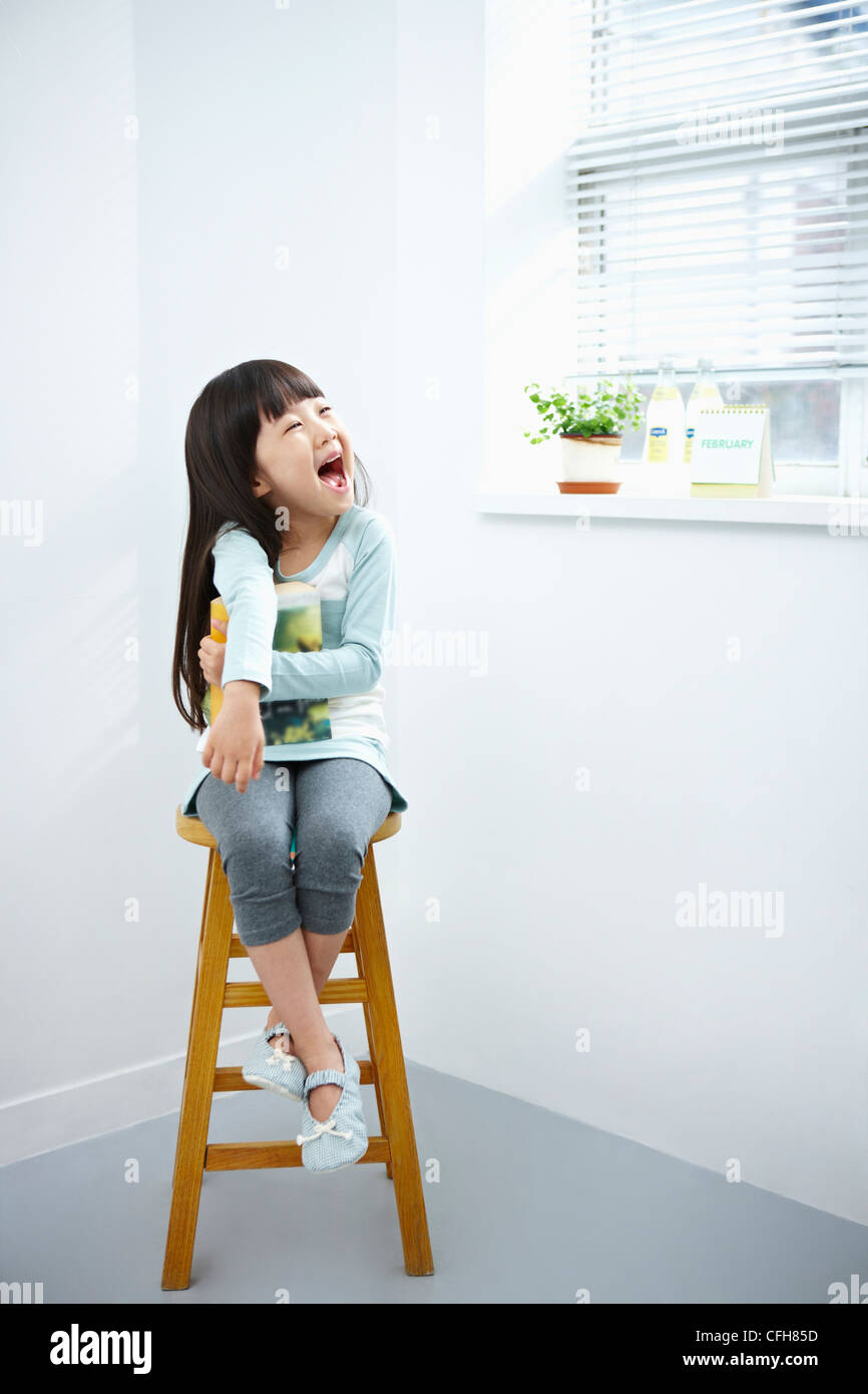 The girl with big smile holding a book on the chair Stock Photo - Alamy