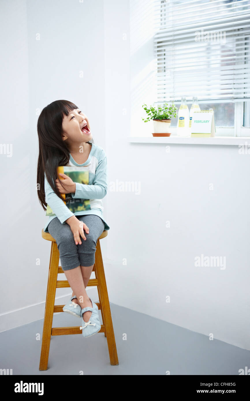 The girl with big smile holding a book on the chair Stock Photo - Alamy