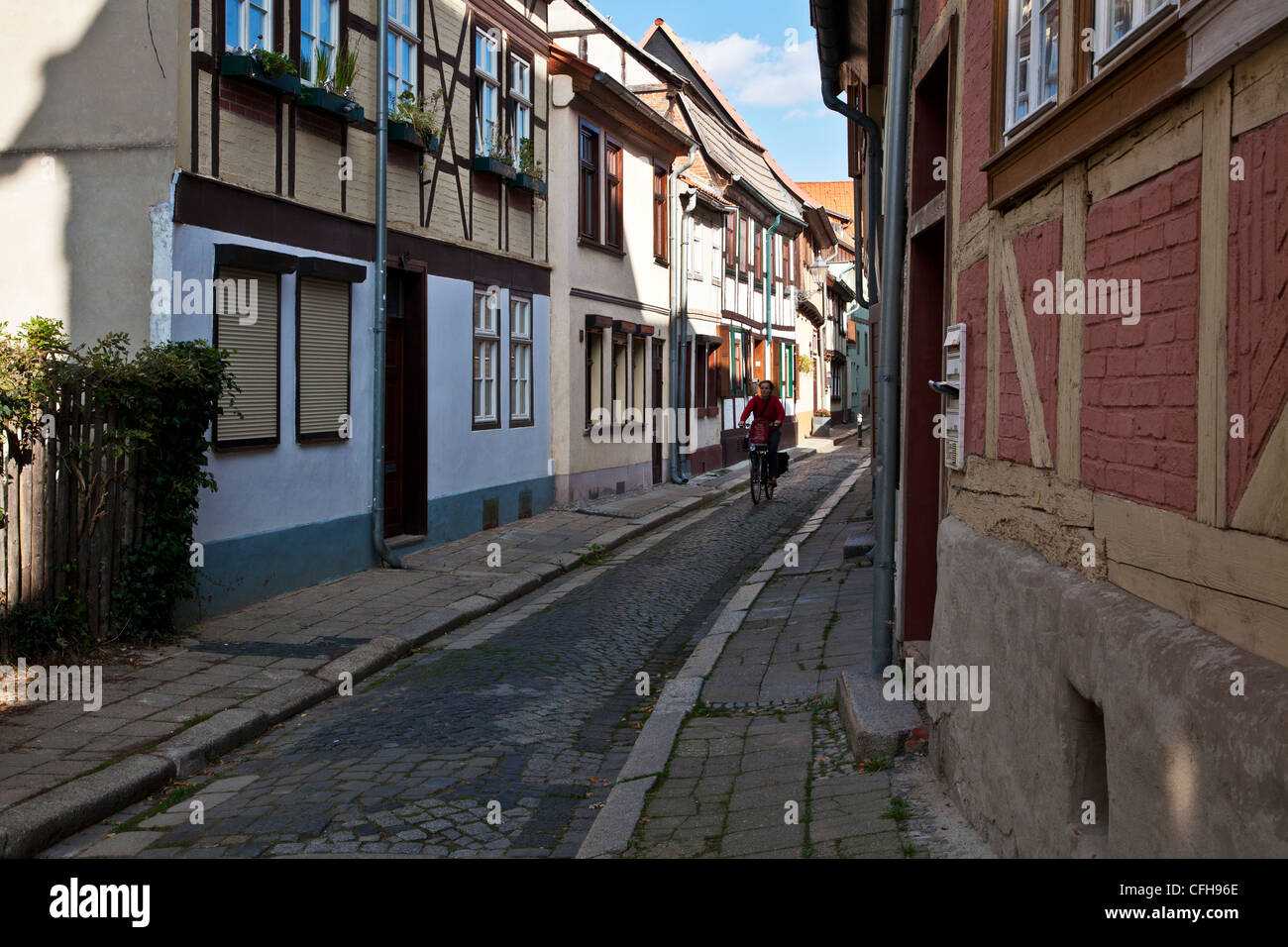 Woman cycling down a narrow cobbled street in the UNESCO German town of Quedlinburg, Saxony-Anhalt, Germany, EU Stock Photo