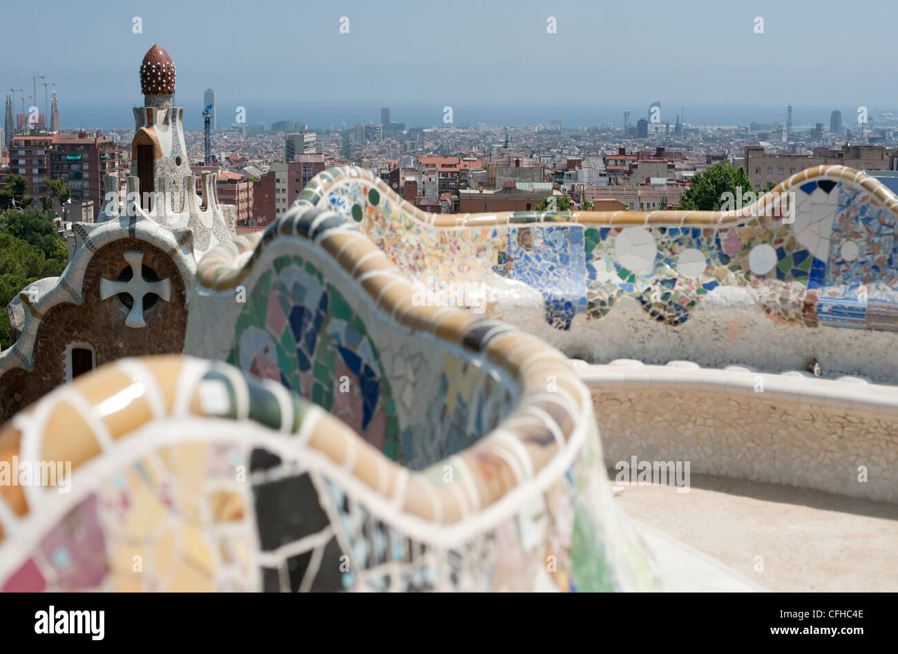 The sea serpent tiled mosaic bench in the main terrace of Park Guell with Barcelona in the distance. Stock Photo