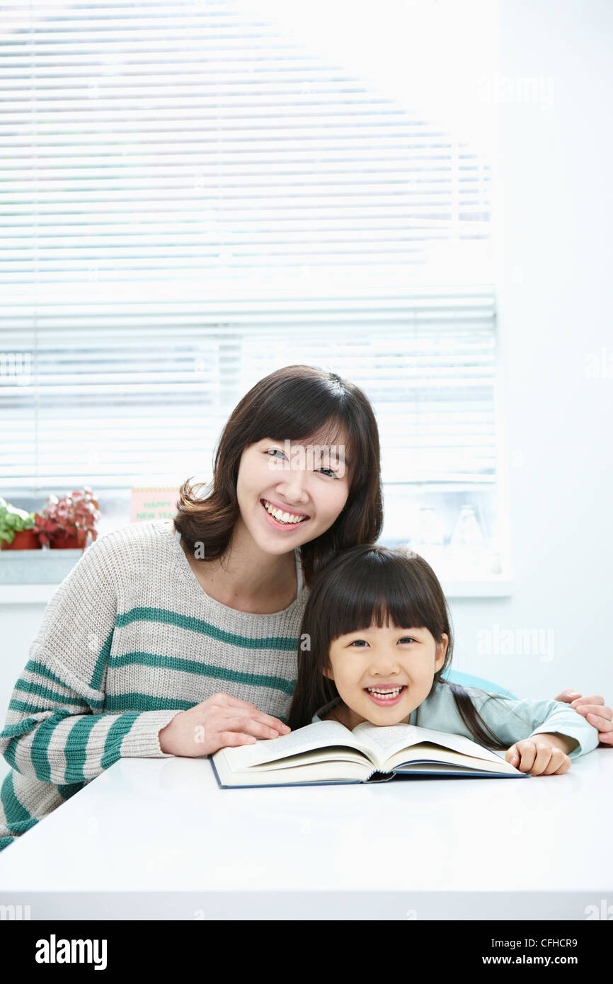 A smiling woman and girl with a book on the desk Stock Photo - Alamy