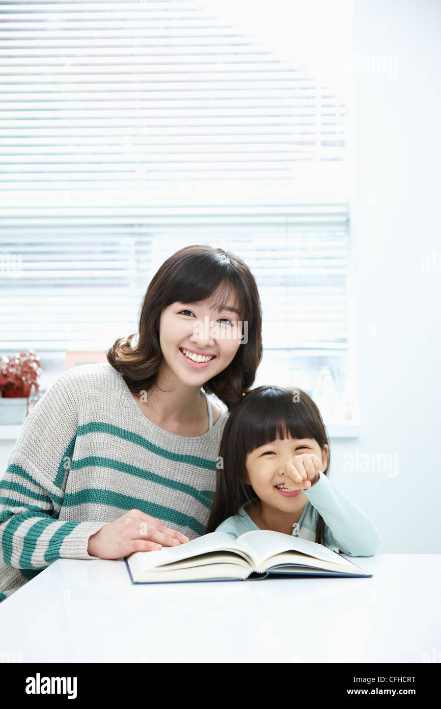 A smiling woman and girl with a book on the desk Stock Photo - Alamy