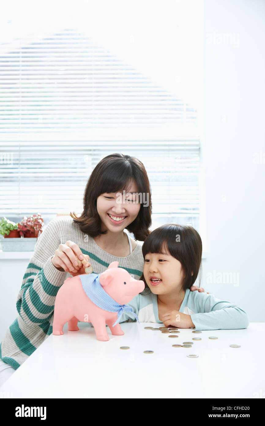 A woman and girl putting a coin into a pink piggy bank Stock Photo - Alamy