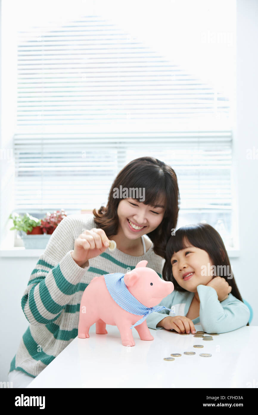 A woman and girl putting a coin into a pink piggy bank Stock Photo - Alamy