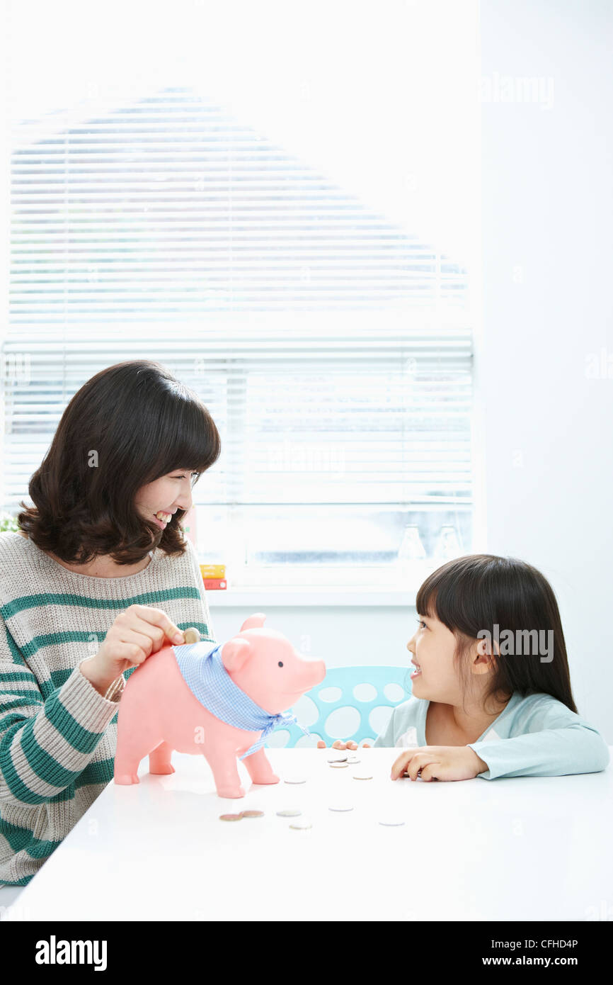 A woman and girl putting a coin into a pink piggy bank Stock Photo - Alamy