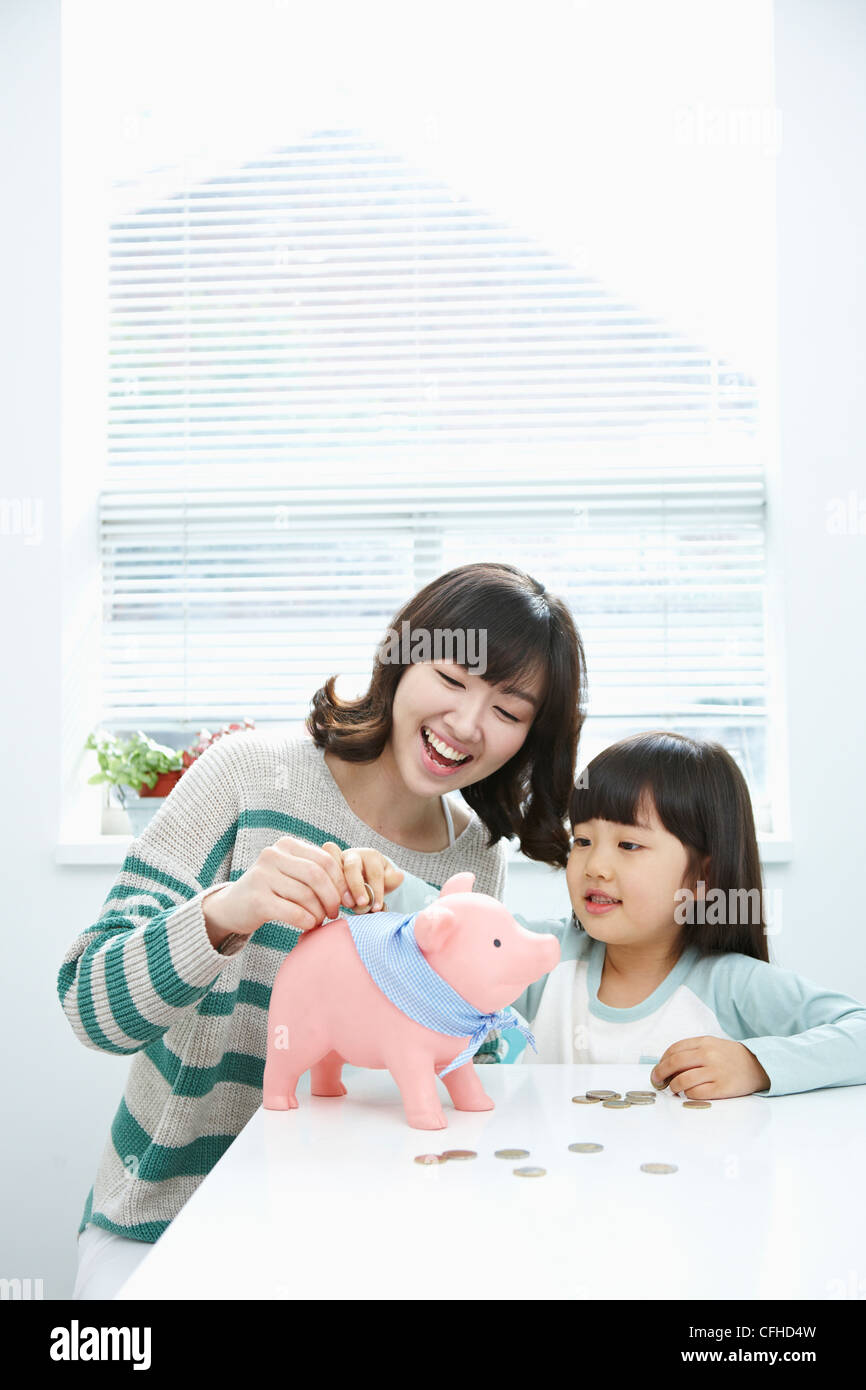 A woman and girl putting a coin into a pink piggy bank Stock Photo - Alamy