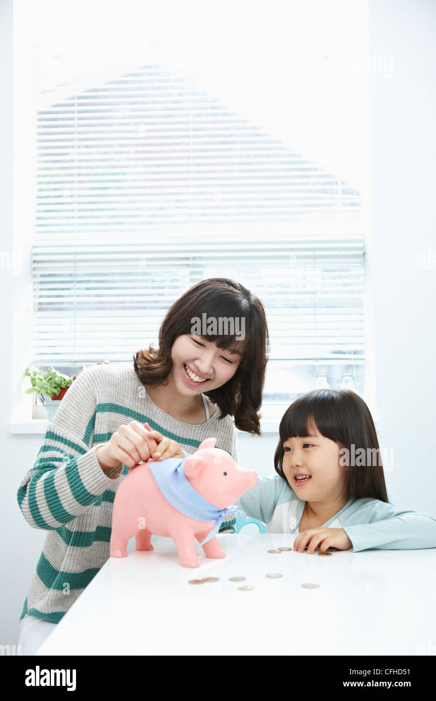 A woman and girl putting a coin into a pink piggy bank Stock Photo - Alamy