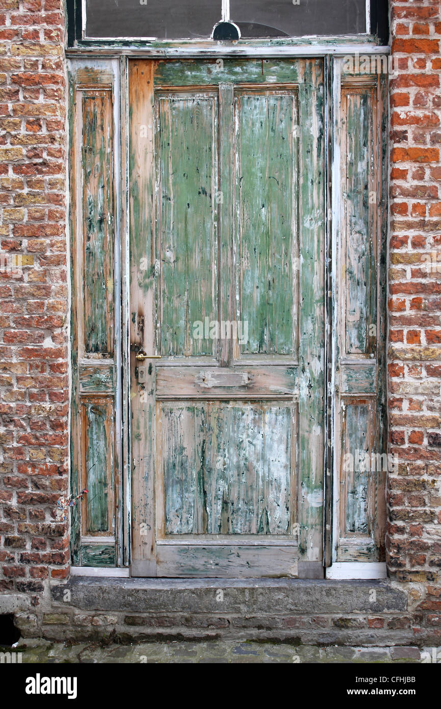 A green door with peeling paint set in a red brick wall Stock Photo Alamy
