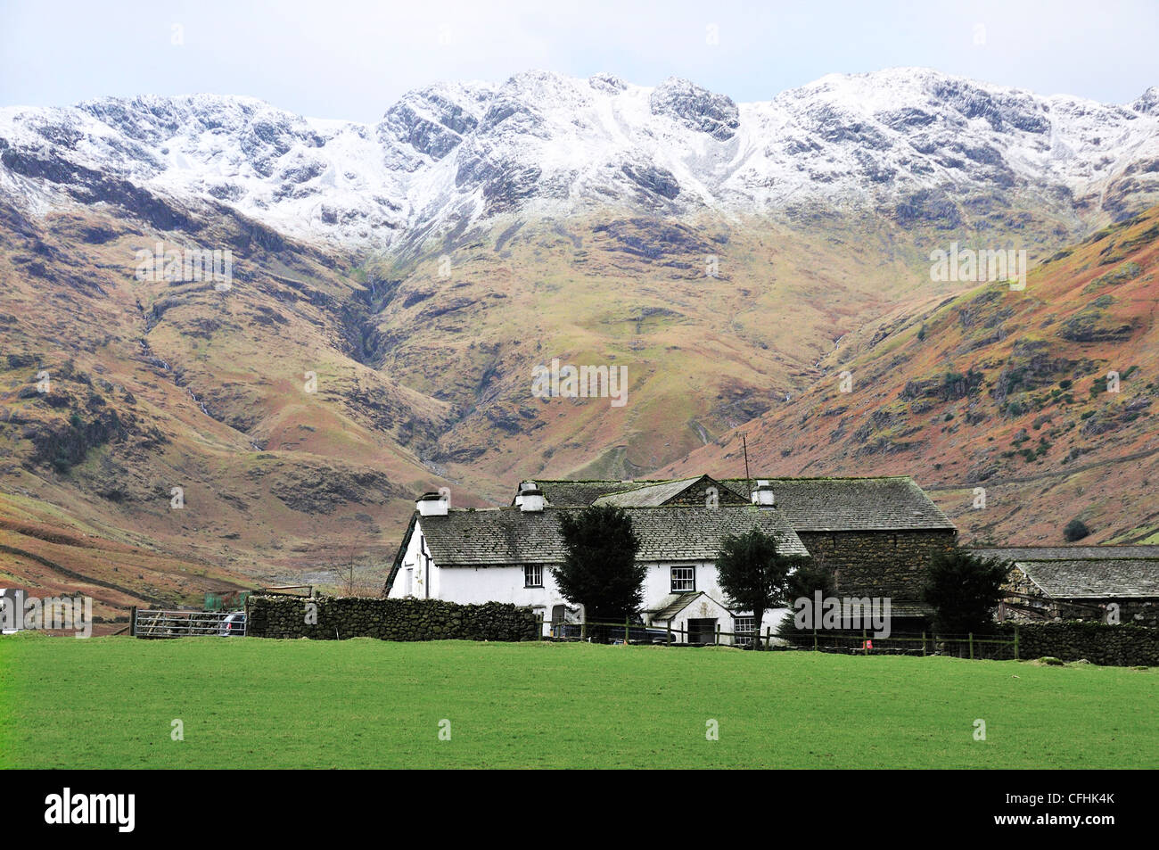 Farmhouse with snow capped Langdale Pikes in background at the end of the Langdale Valley, Great Langdale, Lake District, Cumbria, England, UK Stock Photo