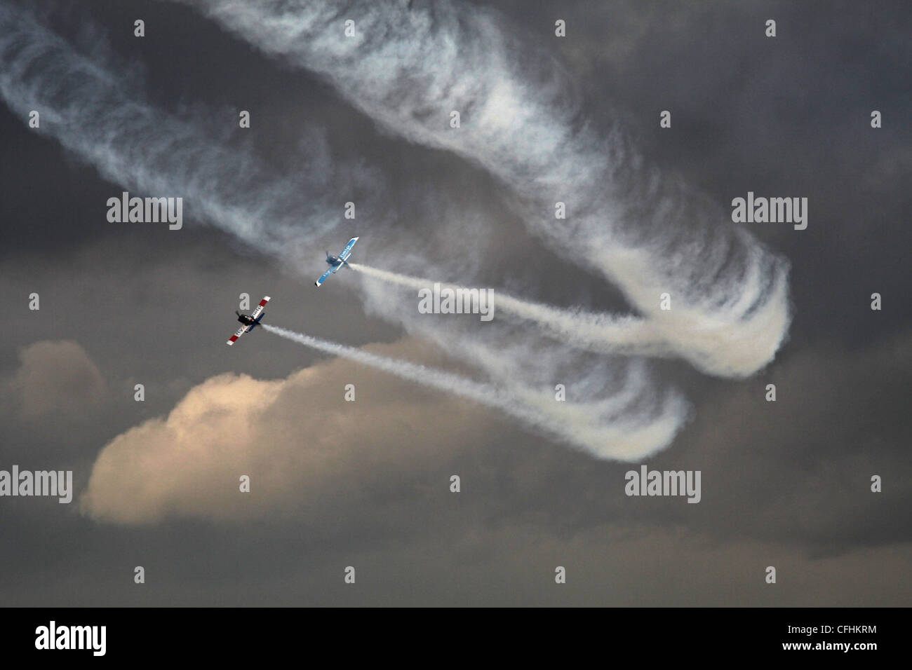 two planes leave a trail of smoke against the backdrop of dark skies during an air display at leuchers airshow Stock Photo