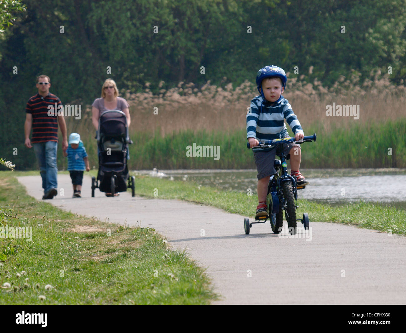 Little boy on his bike followed by his family, Bude, Cornwall, UK Stock Photo