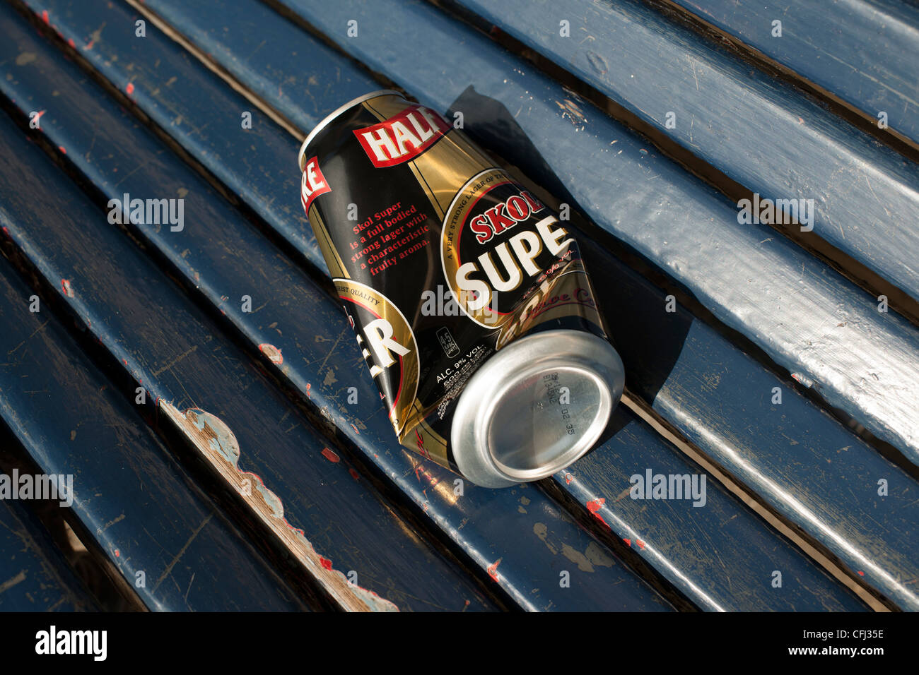An empty and semi-crushed beer can lies on a blue wooden seat of a park shelter where is was abandoned by the drinker. Stock Photo