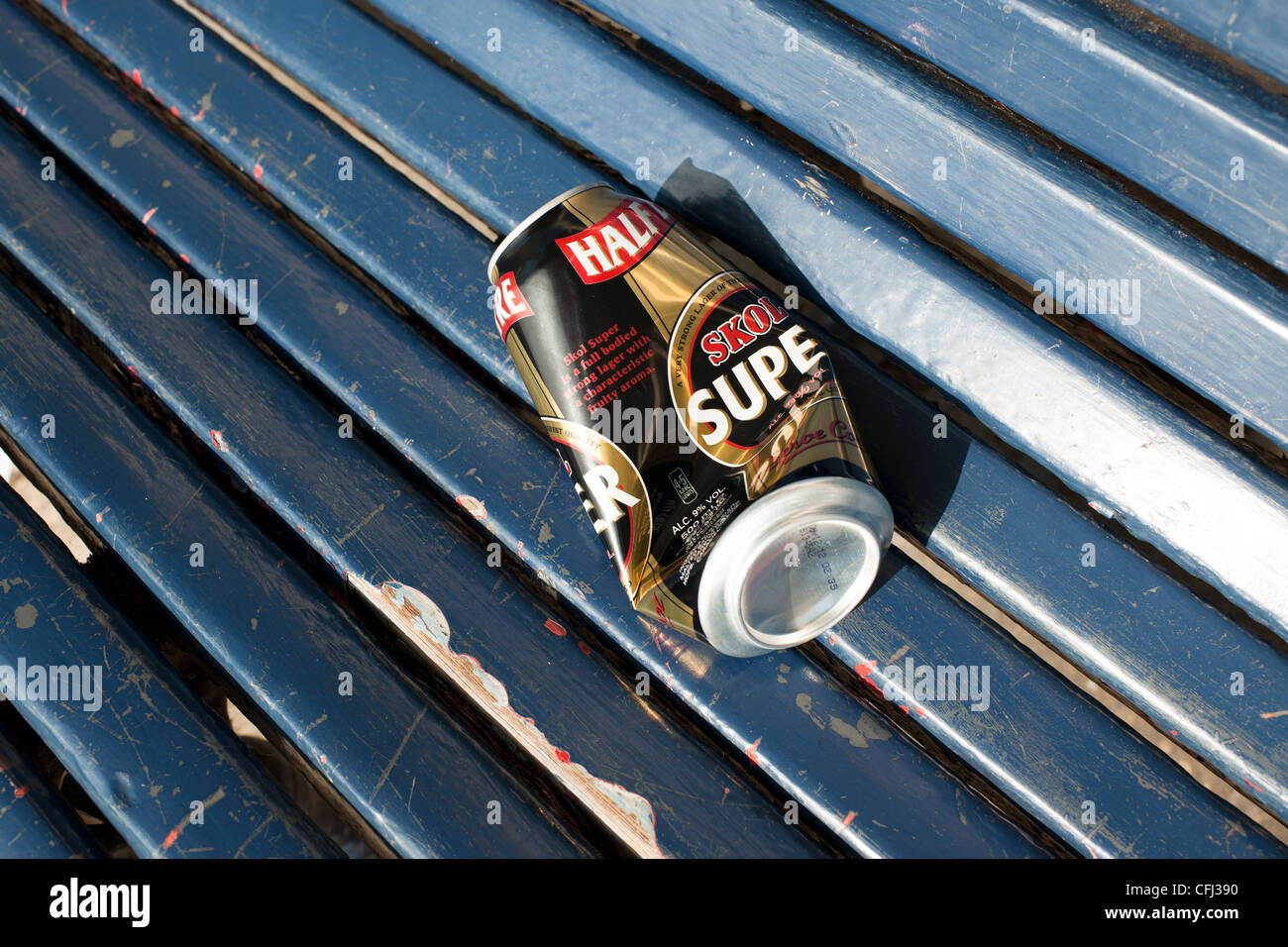 An empty and semi-crushed beer can lies on a blue wooden seat of a park shelter where is was abandoned by the drinker. Stock Photo