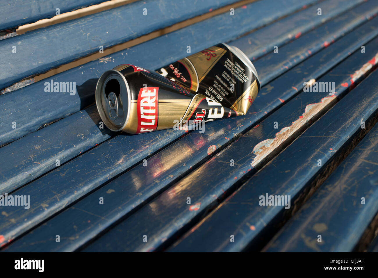 An empty and semi-crushed beer can lies on a blue wooden seat of a park ...