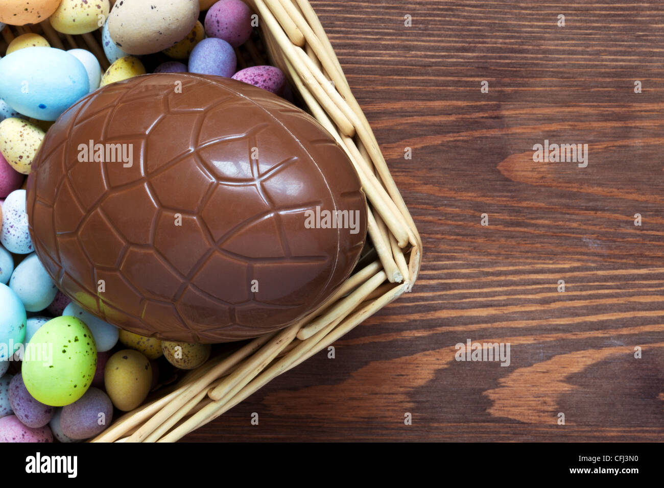 Still life photo of a large chocolate easter egg in a basket surrounded by candy covered mini eggs Stock Photo