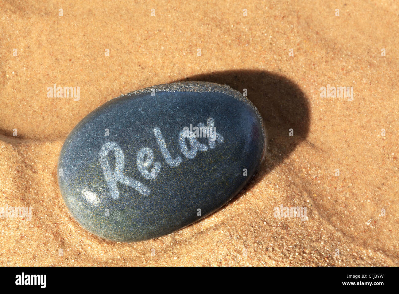 Concept photo of a wet pebble on the beach with the word Relax on it with the late setting sunshine casting a shadow. Stock Photo