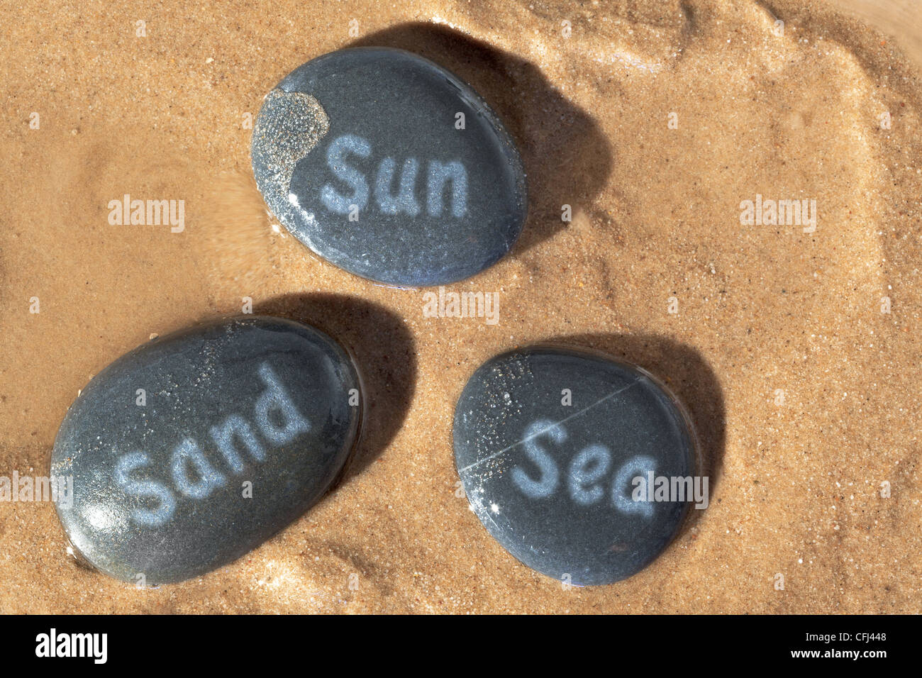 Concept photo of Sun Sand and Sea written on wet pebbles on the beach with the sunshine casting deep shadows. Stock Photo