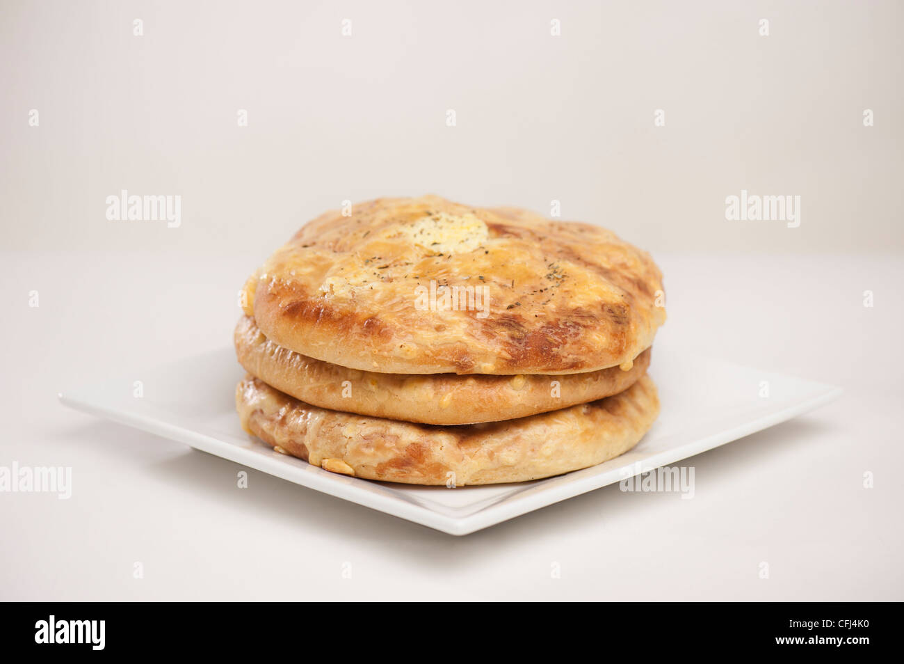 Khachapuri – a filled bread dish from Georgia. On round, white plate and light, clean background. Stock Photo