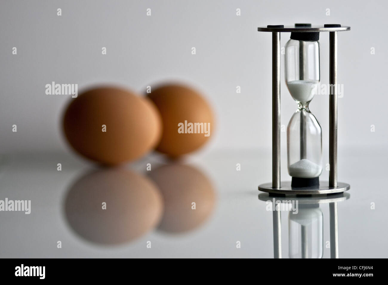 Eggs and an egg timer on a reflective surface. Stock Photo