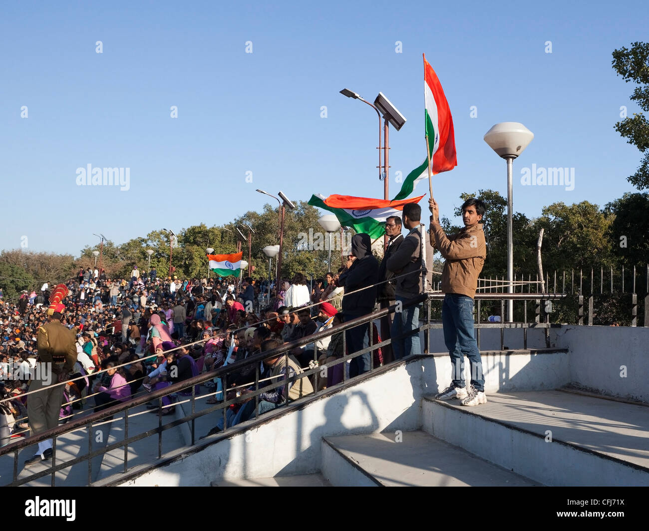 a young man proudly waves the Indian flag as crowds of tourists watch the famous Wagah border ceremony in Punjab India Stock Photo