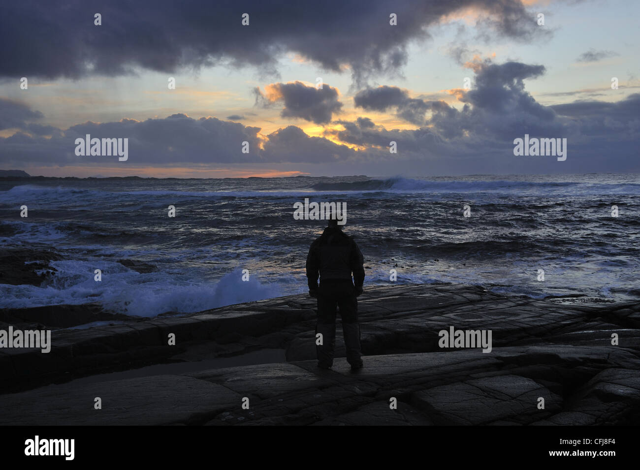 Man standing on rocks looking out to sea in sunset Stock Photo - Alamy