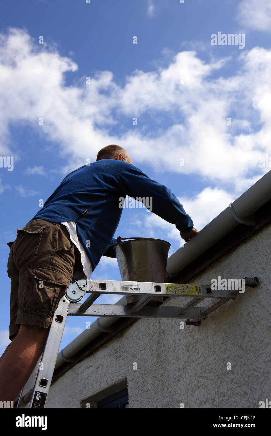 Man up a ladder cleaning the gutters on a cottage Stock Photo - Alamy