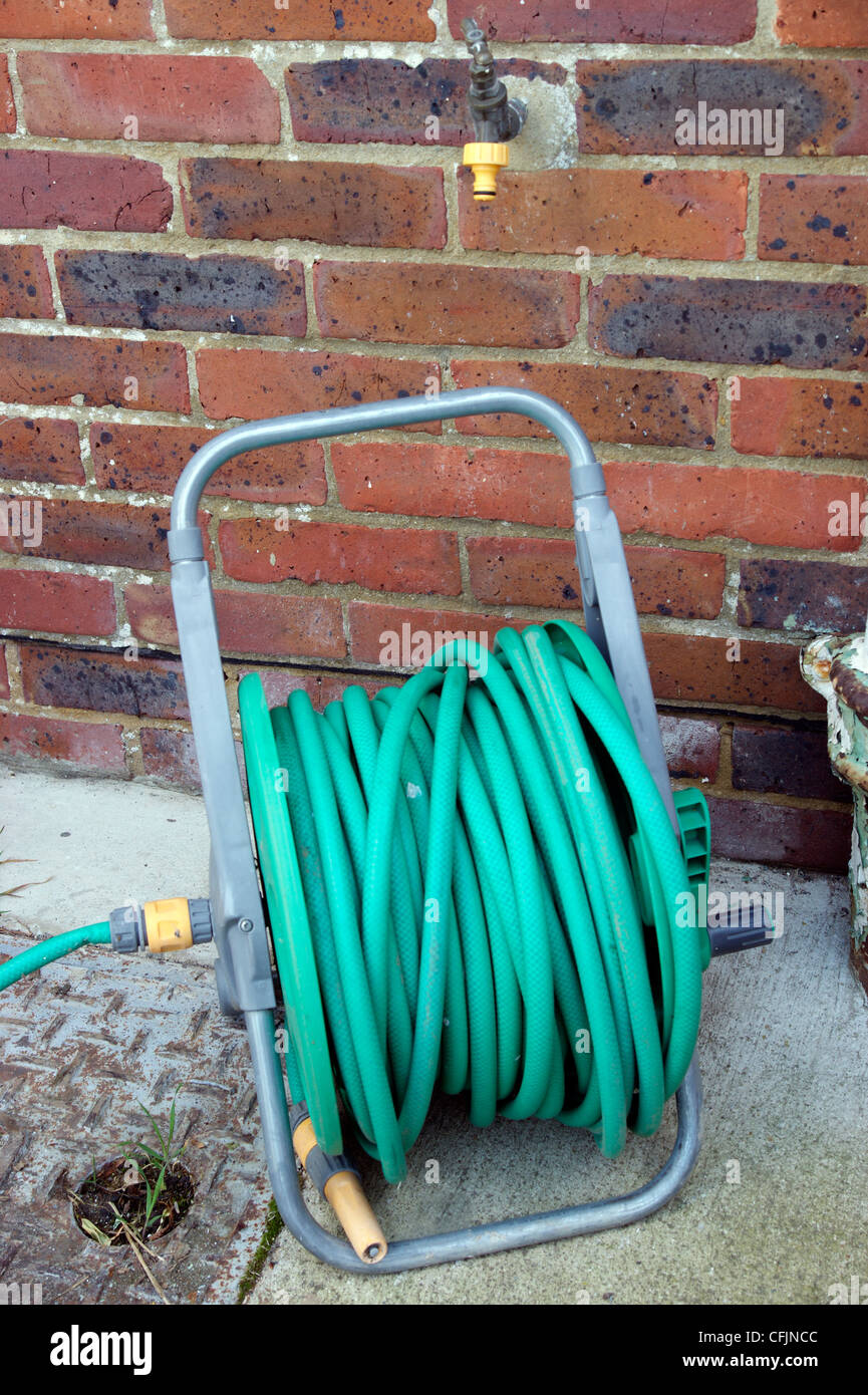 Hose pipe on a reel in garden laying dormant with the hosepipe ban in force in many areas of the country near outside tap Stock Photo