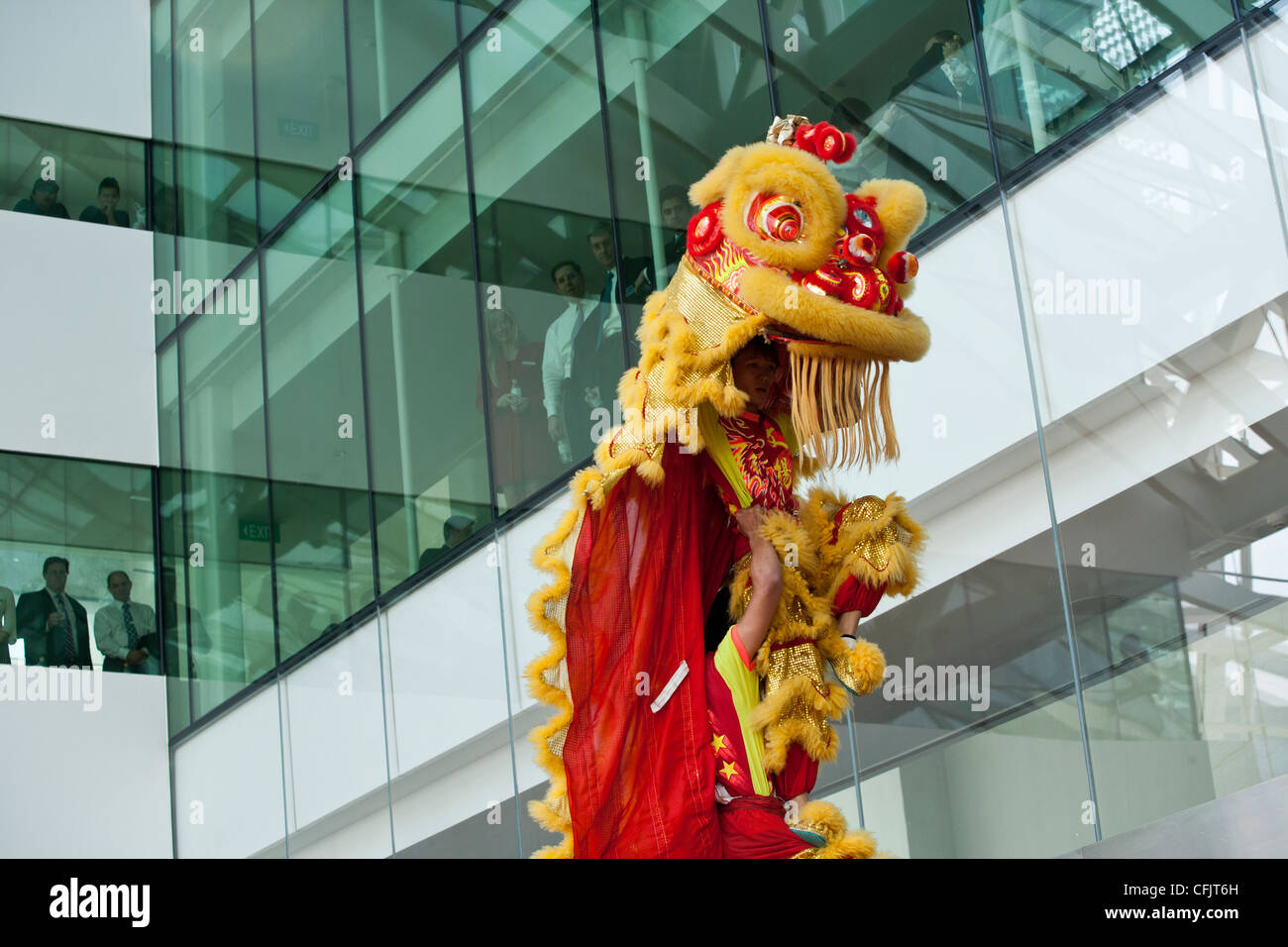 Lion Dancers perform as office workers look on from a window in and office building in Singapore. Stock Photo