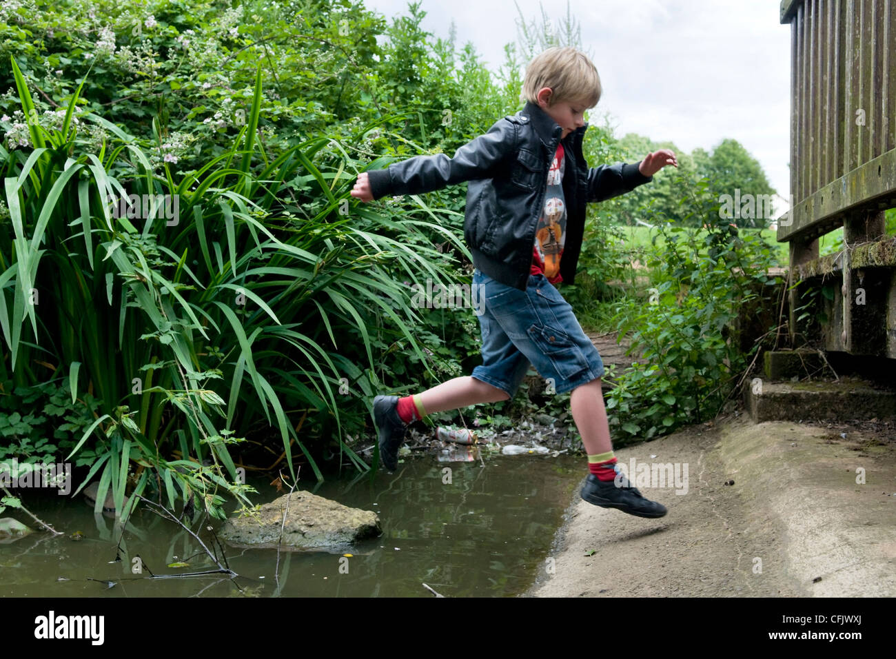 8 year old Caucasian boy jumping over rocks in stream at Barrs Court
