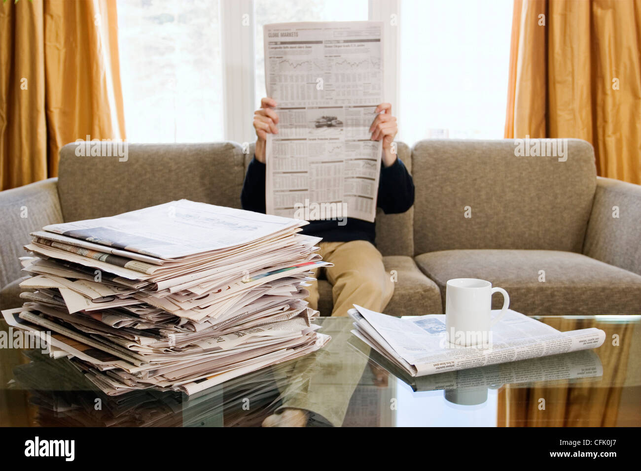 Man Sitting on Couch Reading from Stack of Newspapers Stock Photo - Alamy