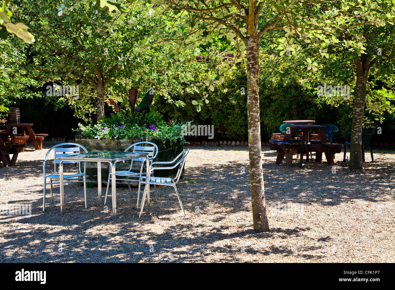 Cafe tables in dappled shade of  trees on gravel patio in English country garden of Littlecote Manor in Berkshire, England, UK Stock Photo