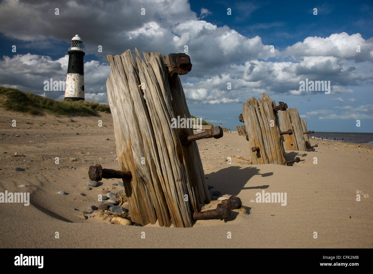 Wooden posts and groynes on the beach in front of the black and white lighthouse at Spurn Point, Yorkshire Stock Photo