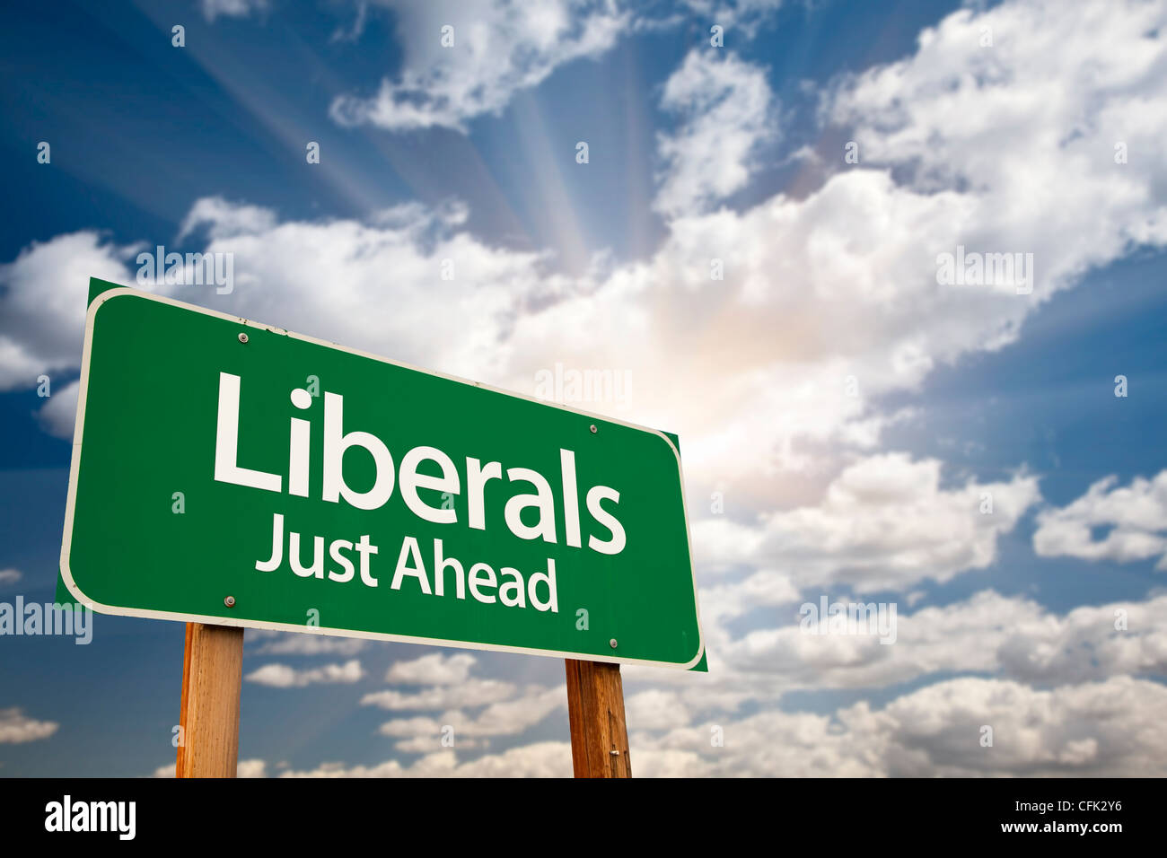 Liberals Green Road Sign with Dramatic Clouds, Sun Rays and Sky. Stock Photo