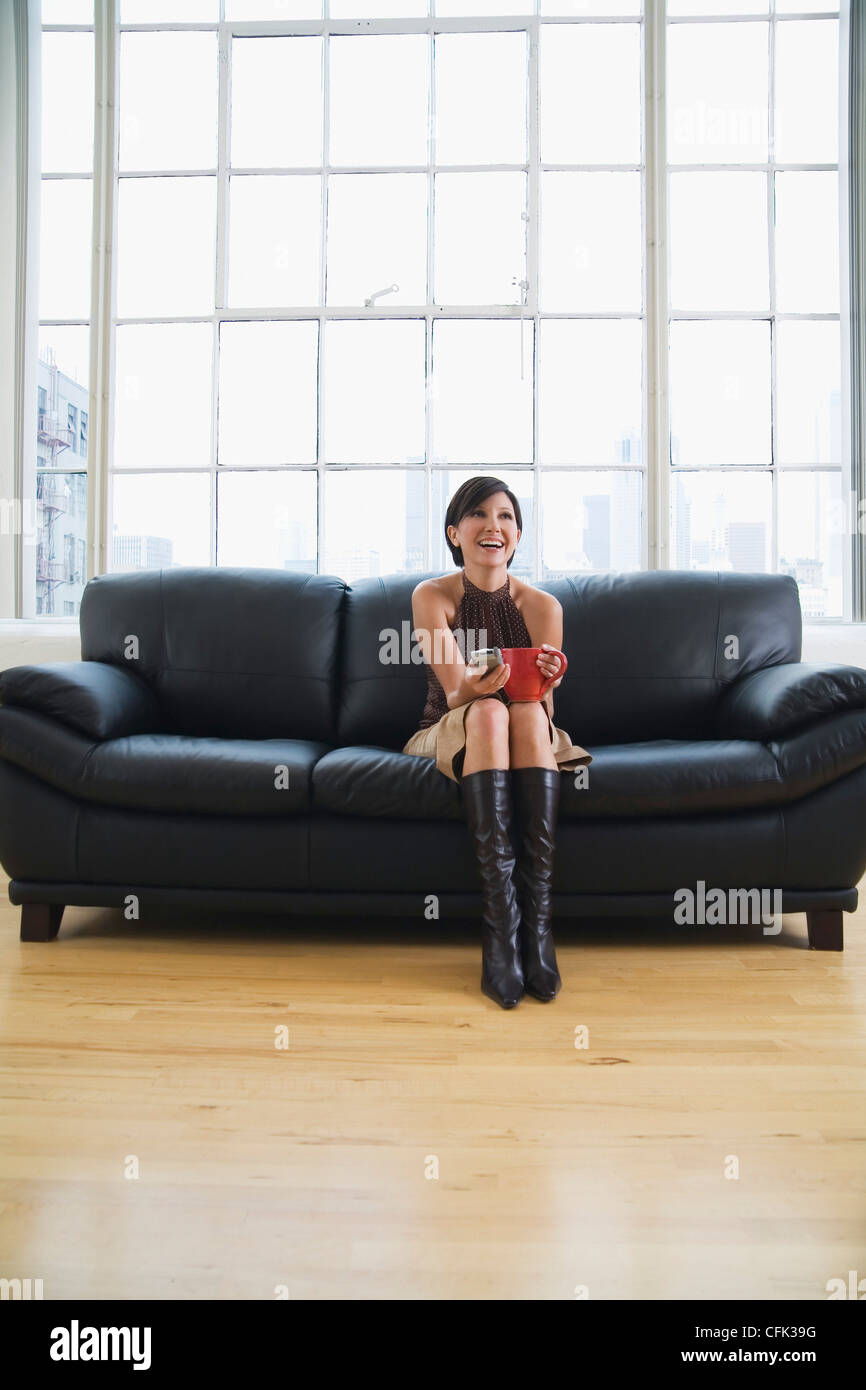 Laughing Woman on Couch holding a Mug and Phone Stock Photo - Alamy