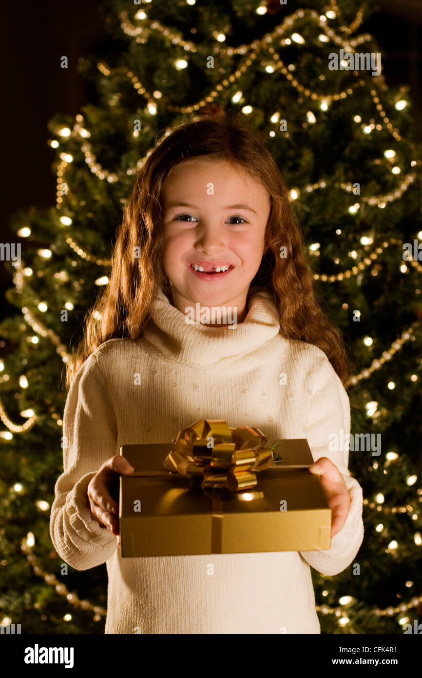 Girl Standing infront of Christmas Tree with a Gift Stock Photo - Alamy