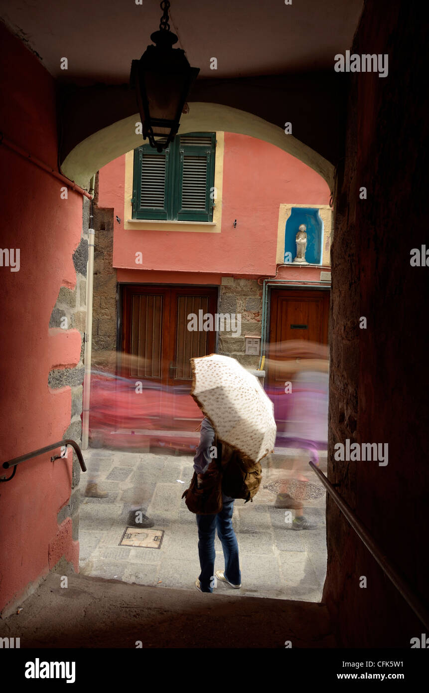 Woman with umbrella standing in street while others stream past. Vernazza, Italy. Stock Photo