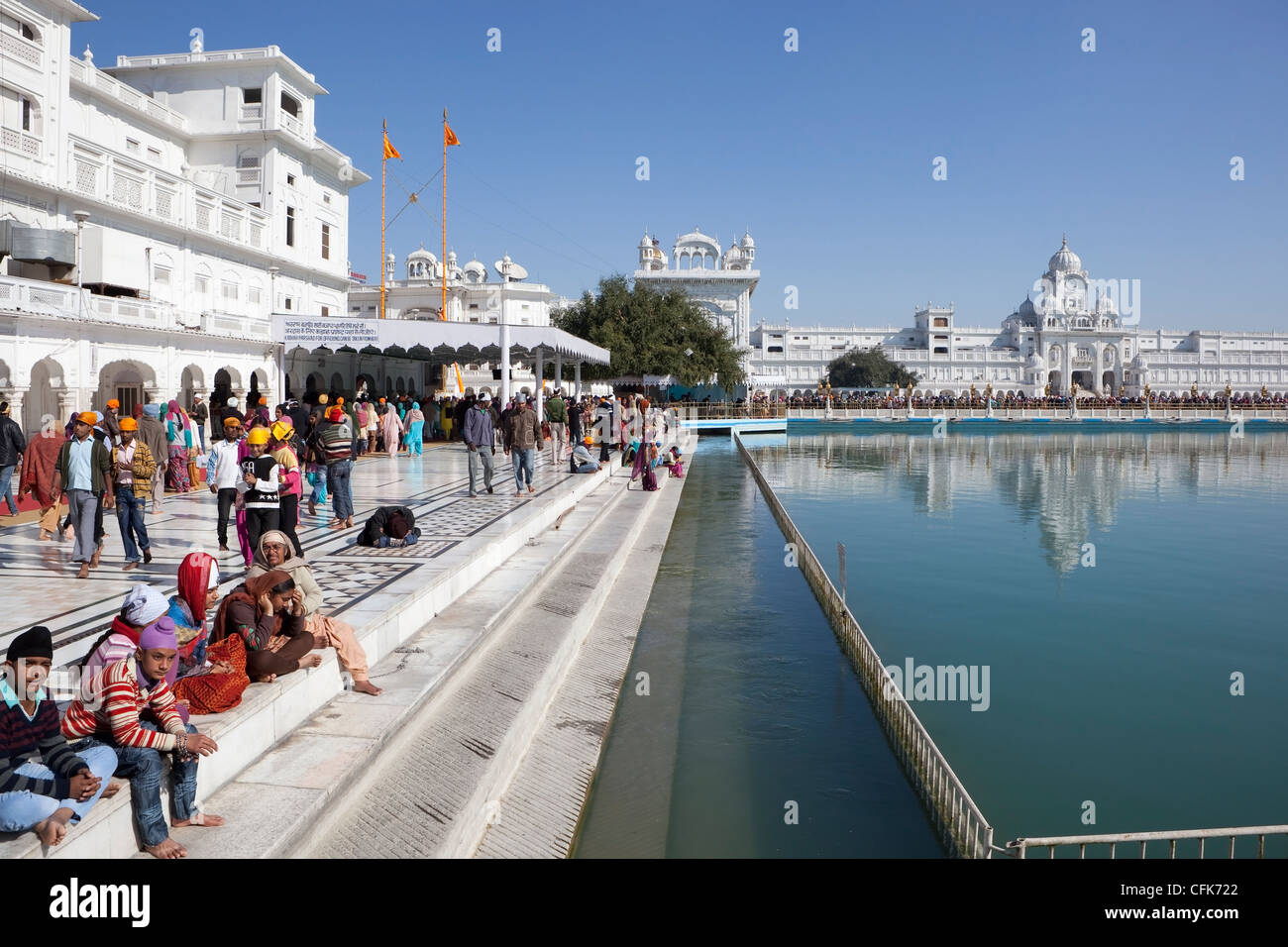 pilgrims walking and sitting around the magnificent golden temple complex in Amritsar Punjab India under a clear blue sky Stock Photo