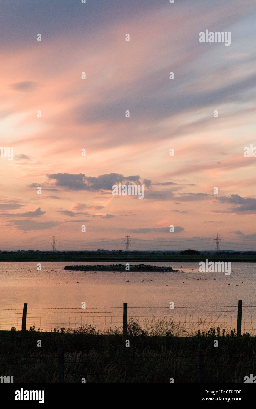 Sunset image with silhouette of fence and pylons over water. Stock Photo