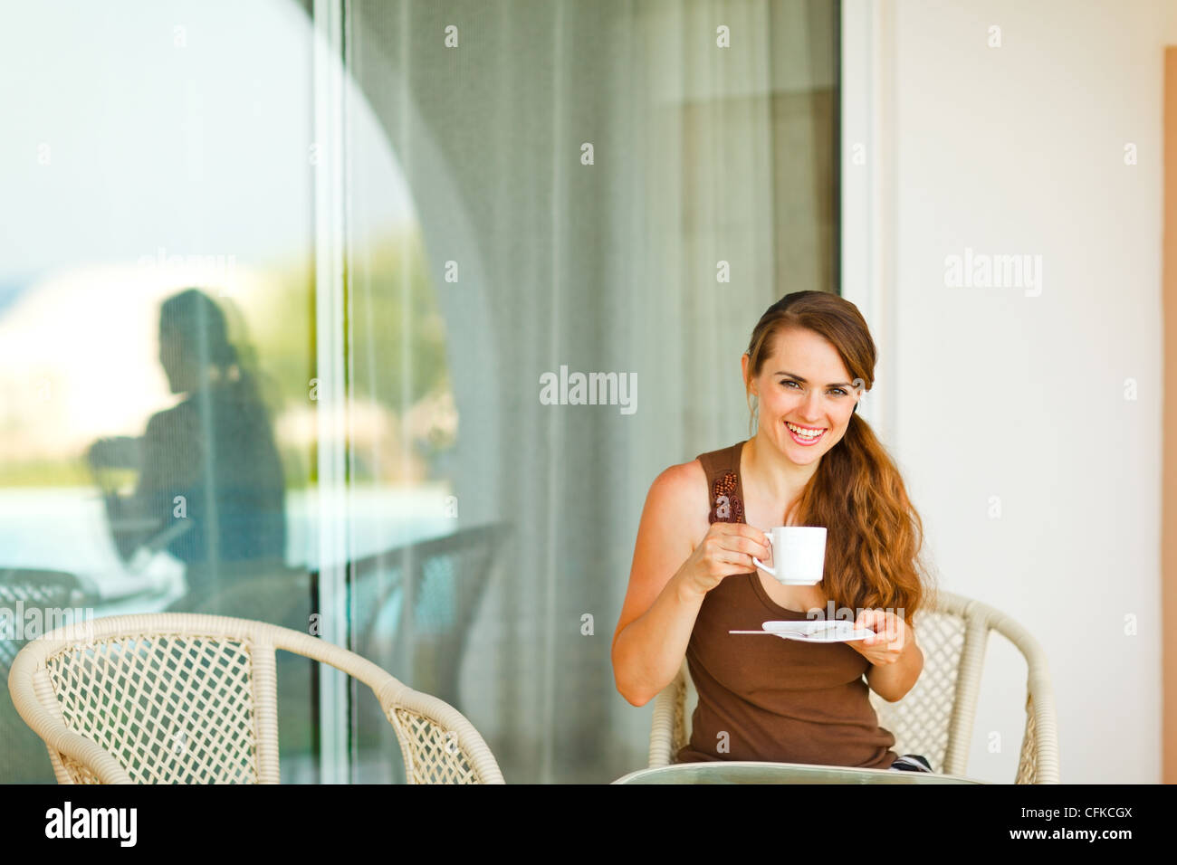 Smiling young woman sitting on terrace and drinking coffee Stock Photo ...