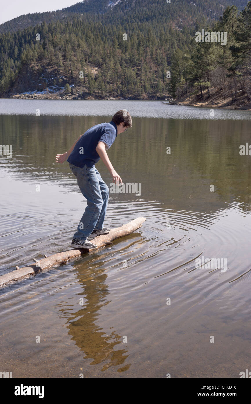 A teenage boy does a balancing act on a floating log, at Bonito Lake in ...