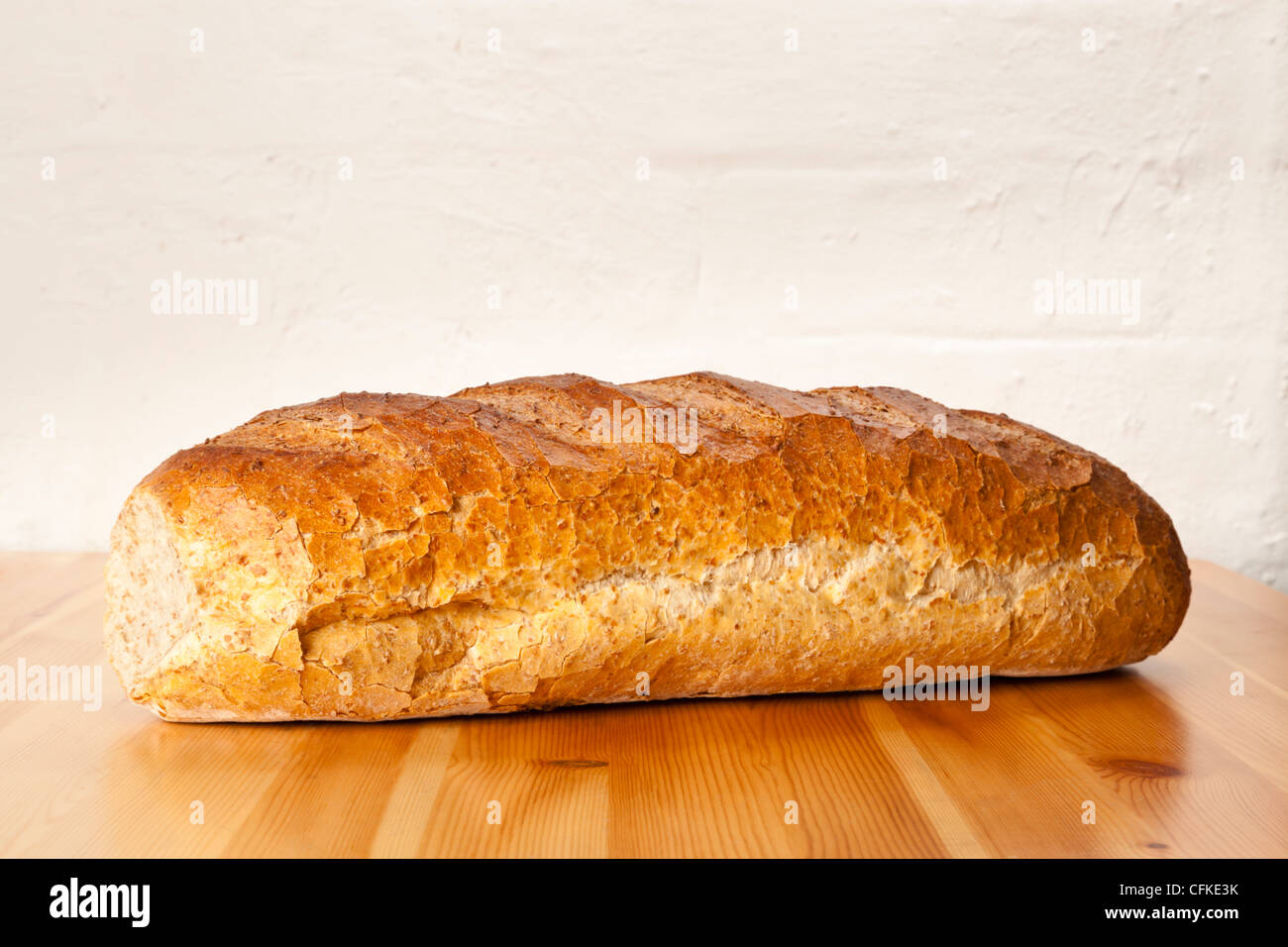 Loaf of brown wholemeal bread on a wooden table against a painted brick wall Stock Photo
