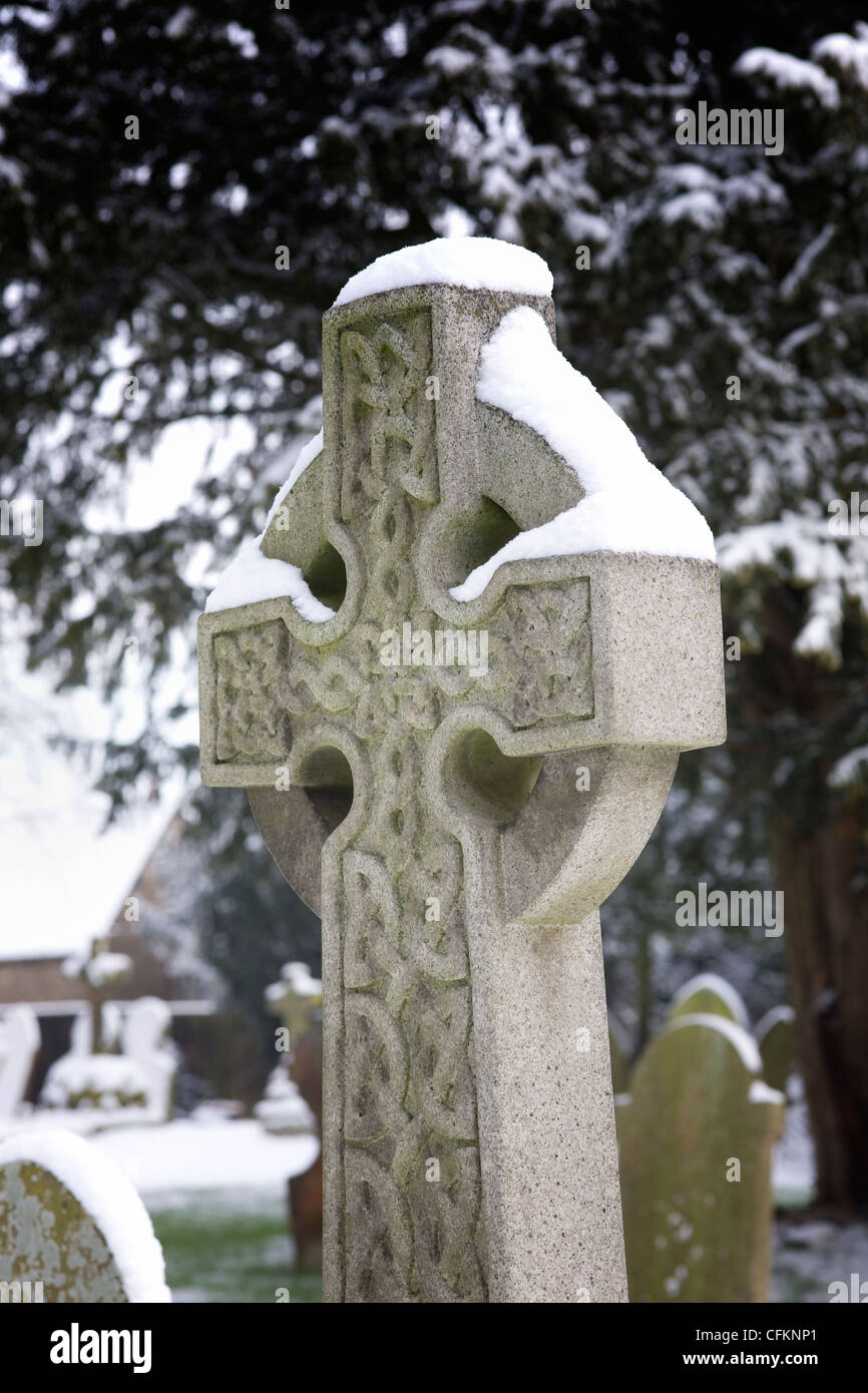Snow lying on a headstone with a celtic pattern, in a churchyard. Stock Photo