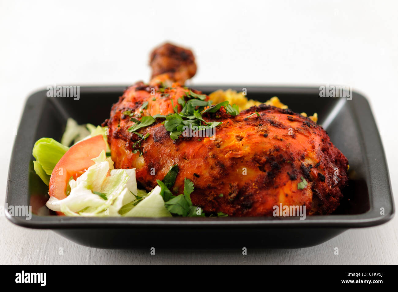 Meal of tandoori chicken leg with saffron rice and salad on black plate garnished with chopped coriander Stock Photo