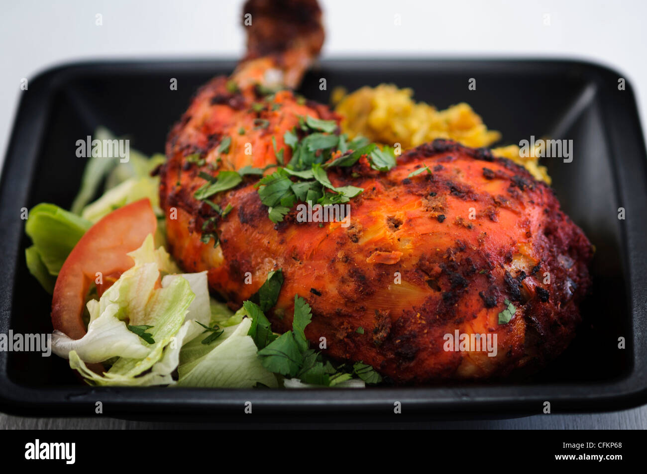 Meal of tandoori chicken leg with saffron rice and salad on black plate garnished with chopped coriander Stock Photo