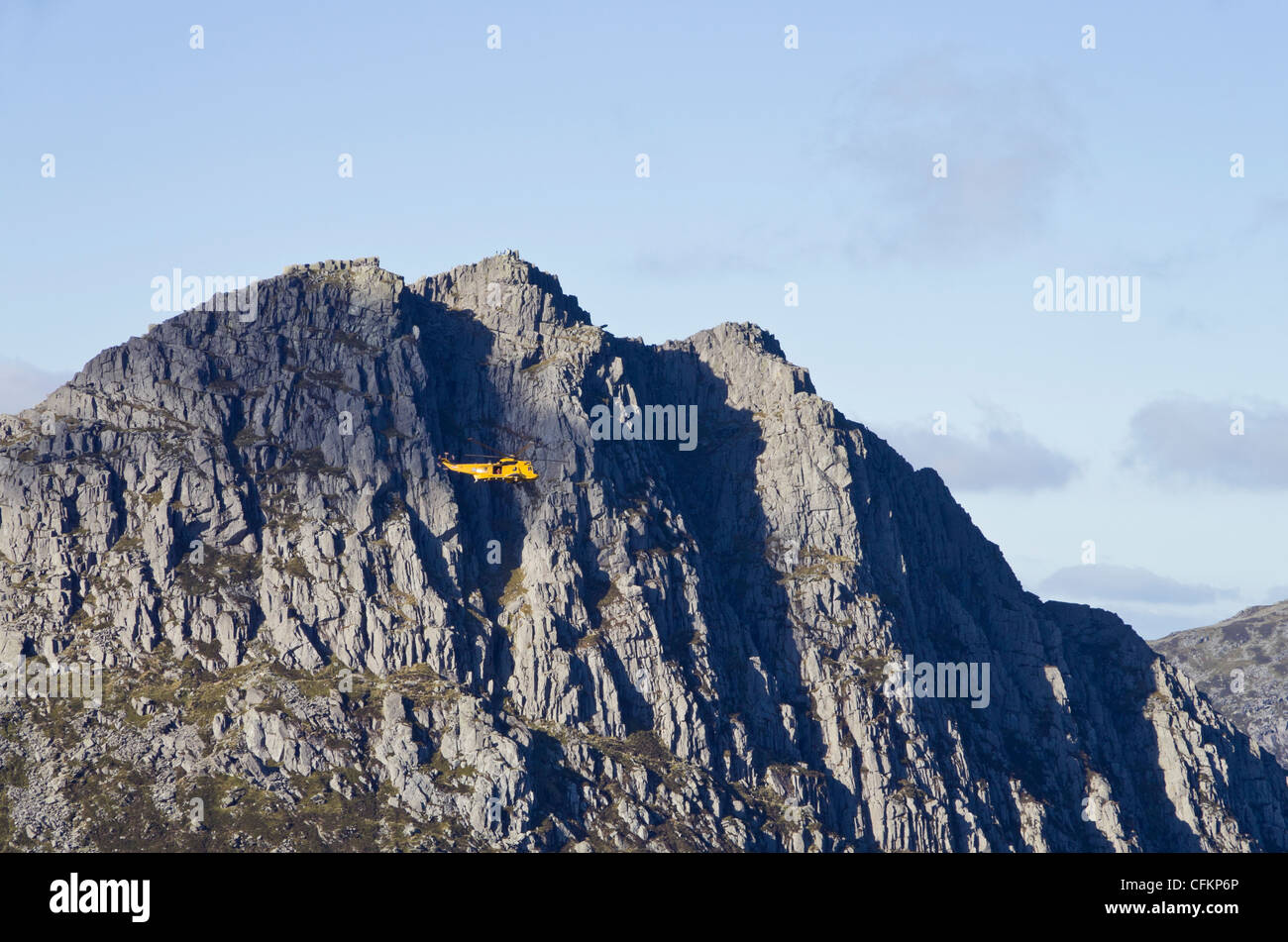Yellow RAF Seaking rescue helicopter hovering near steep crags of Mt Tryfan east face in mountains of Snowdonia North Wales UK Stock Photo