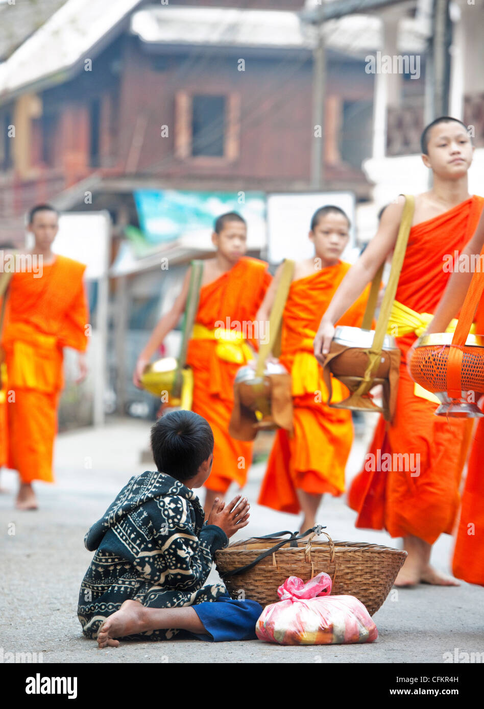 Young boy begging for food from monks who have  been given food at the daily alms giving ceremony in Luang  Prabang, Laos Stock Photo
