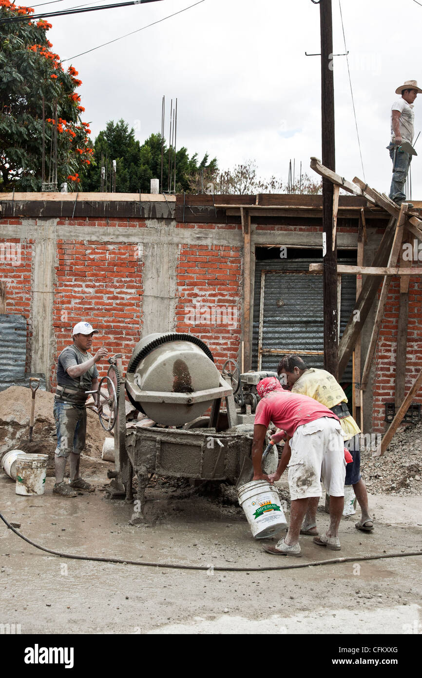 man operates hand powered cement mixer as workmen fill bucket with